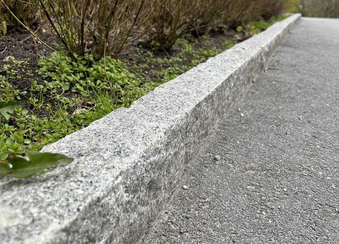 Råkilad kantsten i granit mot plantering i Rosenlundsparken
