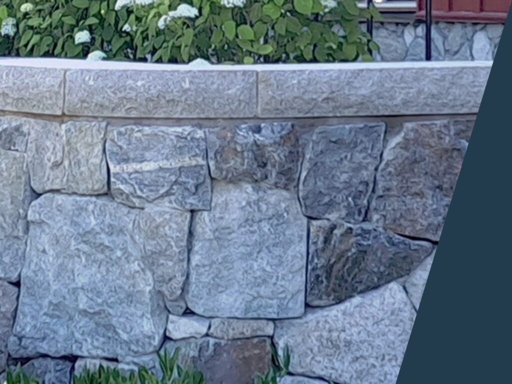 Murkrön i granit på en mur i natursten med planteringar