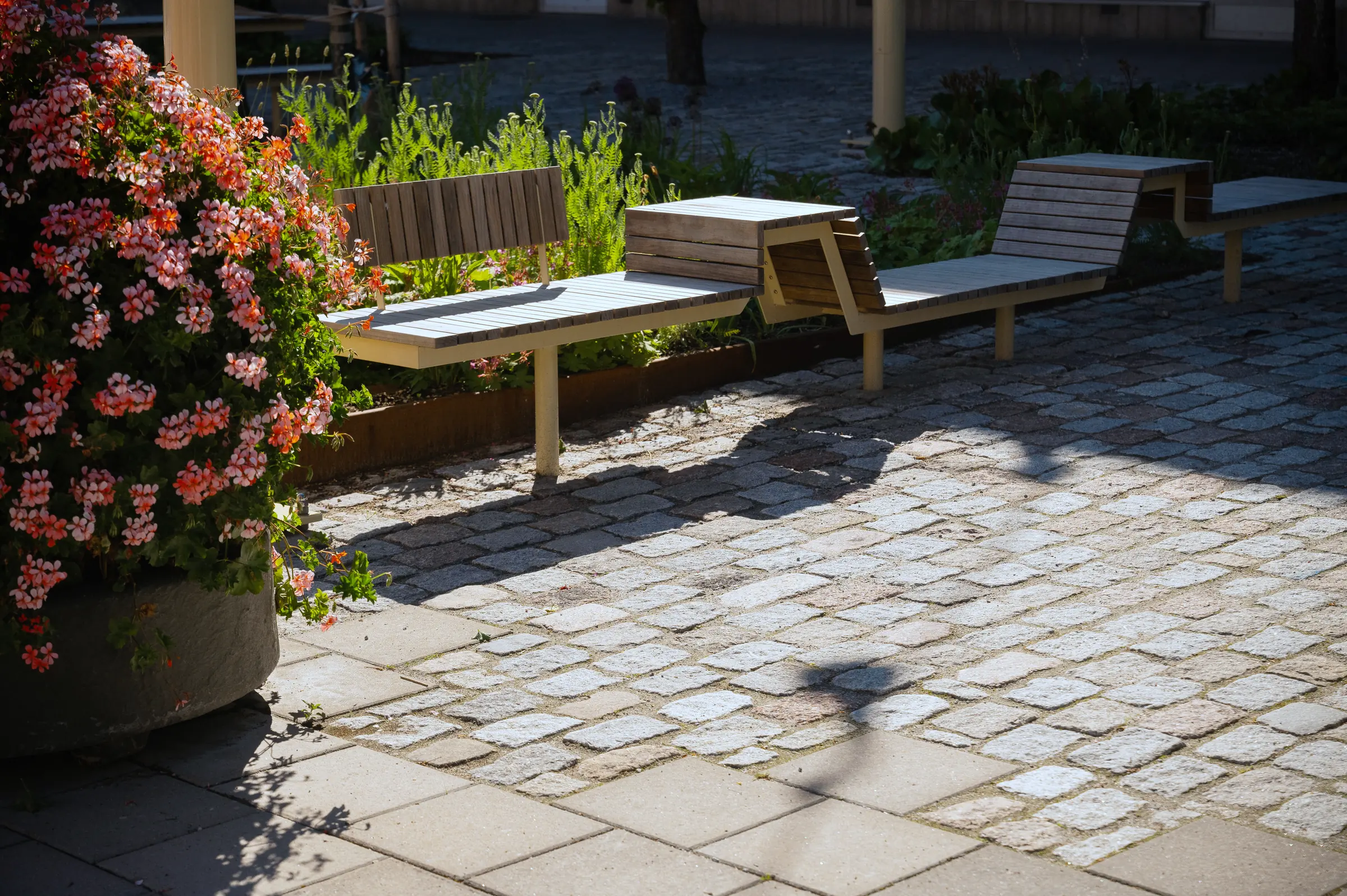 Återbrukad gatsten i grå och röd granit vid bänkar och blommor, Skogås torg